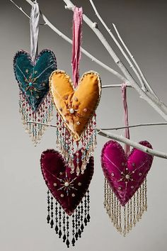 three heart shaped ornaments hanging from a twig with beads and tassels on them