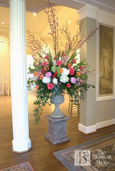 a vase filled with lots of flowers sitting on top of a wooden floor next to pillars