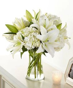 a vase filled with white flowers sitting on top of a table next to a candle