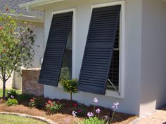 two windows with black shutters on the side of a house in front of flowers