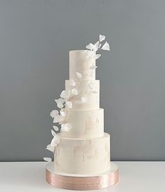 a three tiered white wedding cake with flowers on the top and bottom, in front of a gray background