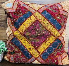 a decorative pillow on a wooden table next to a potted plant and vase with flowers