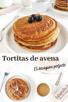 pancakes with blueberries and syrup are on a white plate, next to coffee cups