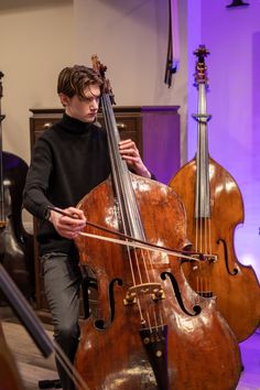 a young man is playing the cello in front of other musical instruments on a stage