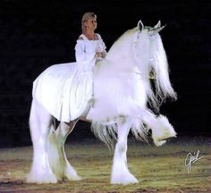 a woman dressed in white riding on the back of a white horse with long hair