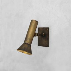 an antique brass wall light on a white stucco wall with a metal cone shade hanging from it's side