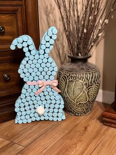 a blue bunny statue sitting next to a vase with twigs in it on a wooden floor