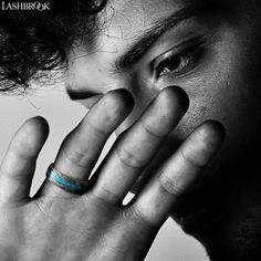 a man holding his hand up to his face while wearing a blue band around his ring