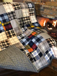 a plaid blanket sitting on top of a wooden floor next to a fire in a fireplace