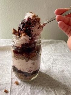 someone is holding a spoon over a dessert in a jar