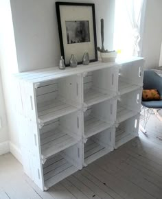 a white bookcase with many shelves and pictures on the top shelf in front of a window