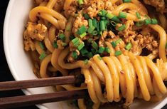 noodles with meat and green onions in a white bowl next to chopsticks on a black surface