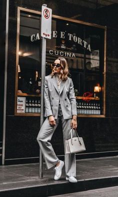 a woman standing in front of a store wearing a gray suit and white shoes with her handbag