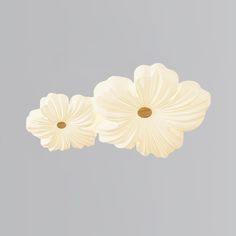 three white flowers hanging from the ceiling in front of a gray wall with light grey background