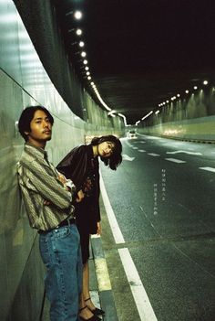 two people standing next to each other on the side of a road at night time