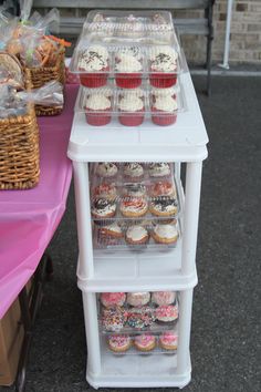 cupcakes and muffins are displayed in plastic containers on a pink table