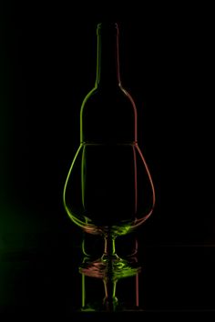 a green wine bottle sitting on top of a table next to a glass filled with liquid