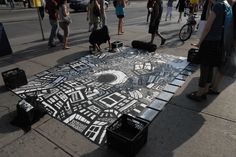 a group of people standing around a large piece of artwork on the sidewalk with luggage