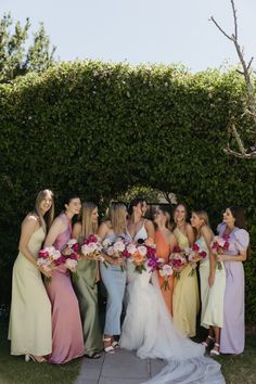 a group of women standing next to each other in front of a lush green hedge