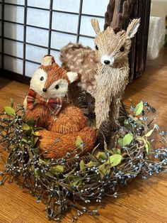 two stuffed animals sitting on top of a wooden floor next to plants and twigs in a basket