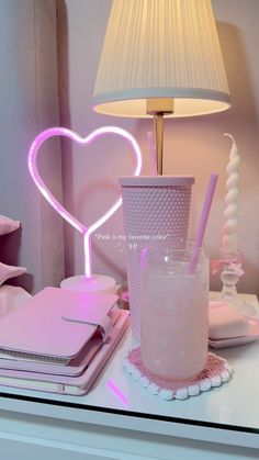 a table topped with a pink heart shaped lamp next to a cup and notebooks