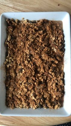 a square white dish filled with granola on top of a wooden table