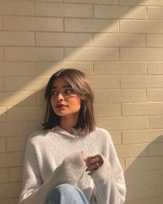 a woman sitting against a brick wall with her hand on her hip