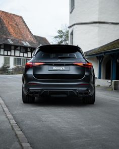 the rear end of a black car parked in front of a white and brown house