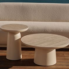 two tables sitting on top of a wooden floor next to a white couch and water