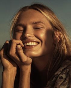 a woman smiling with her eyes closed and hands resting on her chin while looking to the side