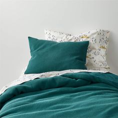 an unmade bed with teal colored sheets and pillows