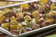 a metal pan filled with potatoes and meat on top of a wooden table next to a green towel