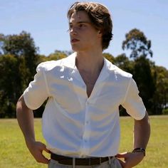 a man standing in the middle of a field with his hands on his hips, wearing a white shirt and khaki pants