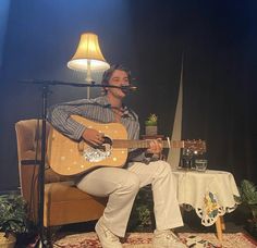 a man sitting on top of a chair holding a guitar in front of a microphone