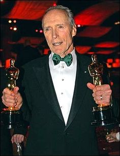 an older man in a tuxedo holding up two oscars for the camera