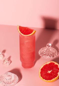 a grapefruit drink in a glass next to two slices of grapefruit