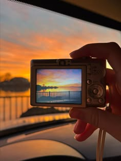 a person holding up a small camera with a sunset in the background