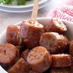 a white bowl filled with cooked sausages on top of a wooden skewer