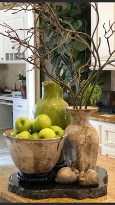 two vases filled with green apples sitting on top of a kitchen counter next to a bowl of fruit