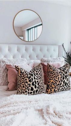 a white bed topped with lots of pillows next to a round mirror on the wall