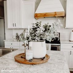 a kitchen with white cabinets and marble counter tops, an oven hood over the stove and a potted plant on a wooden tray