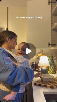 a woman holding a baby in her arms while standing next to a kitchen counter top