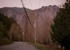 an empty road in the mountains with power lines running through it and trees on both sides