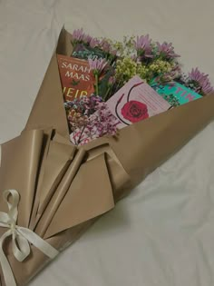 a bouquet of flowers wrapped in brown paper on top of a white sheeted bed