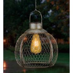 an outdoor light hanging from a chain with chicken wire around it's edges and a yellow light bulb in the center