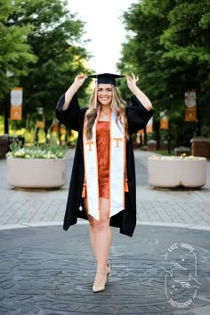 a woman in a graduation gown and cap is posing for the camera with her hands behind her head