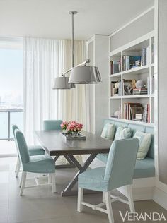 a dining room table with blue chairs next to a book shelf filled with lots of books