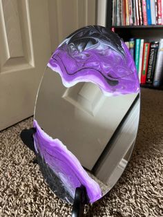 a purple and black mirror sitting on top of a floor next to a book shelf