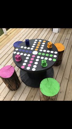 an outdoor table made out of logs and painted with different colors on the top, sitting on a wooden deck