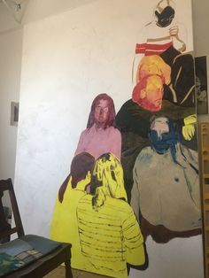 three people standing in front of a wall with paintings on it and one person sitting down